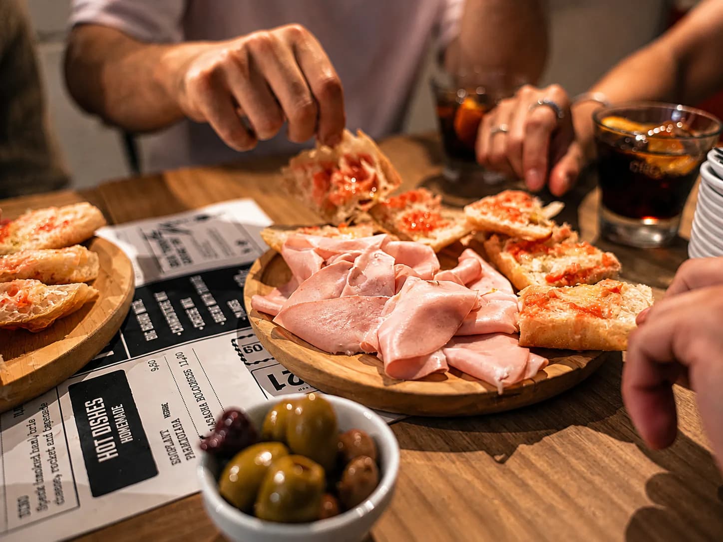 Hands sharing jamón, olives and pan con tomate